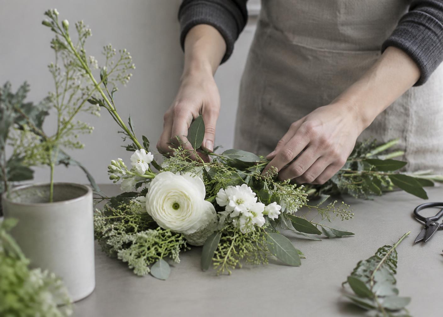 Hender som ordner en enkel dekorasjon med grønt og hvite blomster